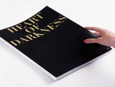 A slim hand with orange nail polish holding a large black book with large gold font reading 