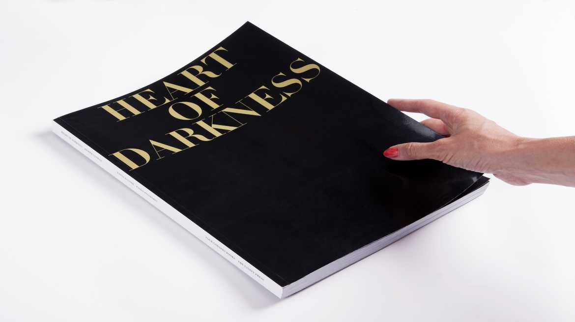 A slim hand with orange nail polish holding a large black book with large gold font reading 