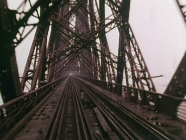 Alia Syed, Points of Departure: A dramatic film still of a muddy red railway bridge made of steel.
