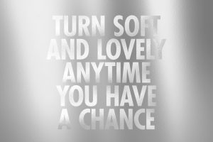Shiny silver metallic centralized text reading 'TURN SOFT AND LOVELY ANYTIME YOU HAVE A CHANCE'