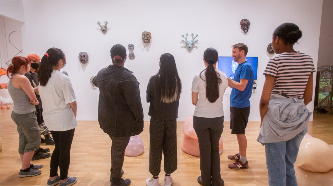 Group of young people seen from behind looking at a wall of sculptural masks