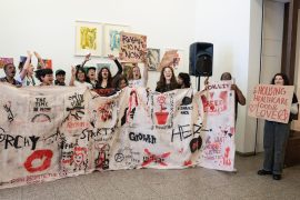 A group of young adults holding a banner with spray painted images and words such as 