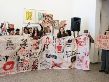 A group of young adults holding a banner with spray painted images and words such as 
