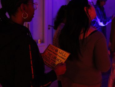 Photo in a darkly lit room of a young person holding a sign saying 