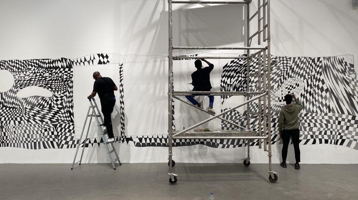Three people in a space painting a black and white geometric mural.
