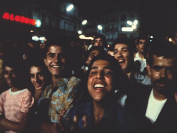 A bustling street of smiling people looking into the camera.