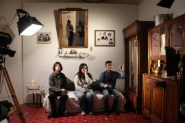 Three young people sit within a scene created by Zineb Sedira