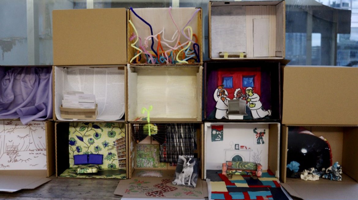 Several cardboard box dioramas of domestic scenes piled on top of each other