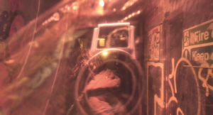 Distorted screenshot from a film showing a graffiti covered alley way through a coloured plastic sheet